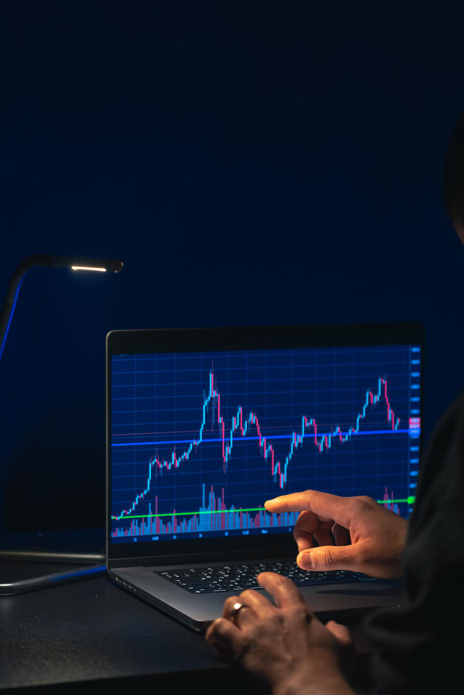 Close-up of a trader pointing at a candlestick chart on a laptop screen, analyzing entry and exit timing strategies for market precision.